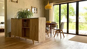 A modern living room with a wooden cabinet, a dining table, and chairs. There is a large window providing a view of greenery outside. - Appartement Contemporain Avec Terrasse à 5mn de du lac D'annecy (Doussard)