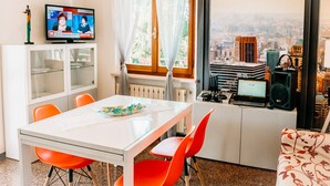 Ein modernes Zimmer mit Esstisch, orangefarbenen Stühlen, einem Fernseher und Blick auf die Stadt.