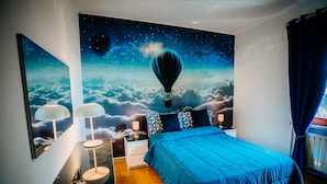 Ein Schlafzimmer mit einem großen Bett, einem Nachttisch, einer Lampe und einer Wandmalerei mit einer Heißluftballon über Wolken.