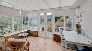 Un luminoso espacio habitable de concepto abierto, con ventanas amplias, piso de madera, sofá blanco, una pequeña mesa redonda y un mueble blanco.