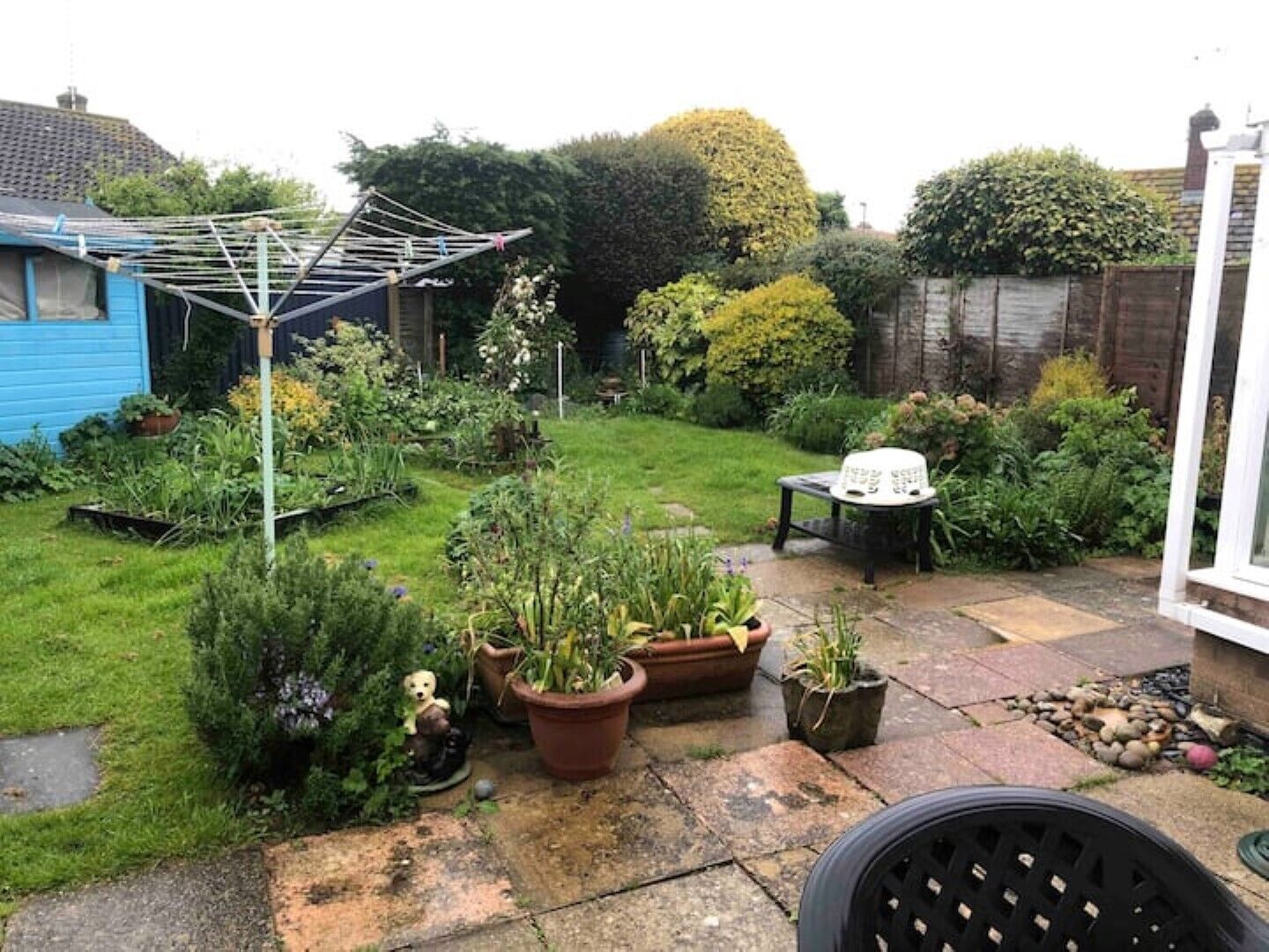 Un jardín con una pérgola, plantas en macetas, una mesa pequeña y un banco.