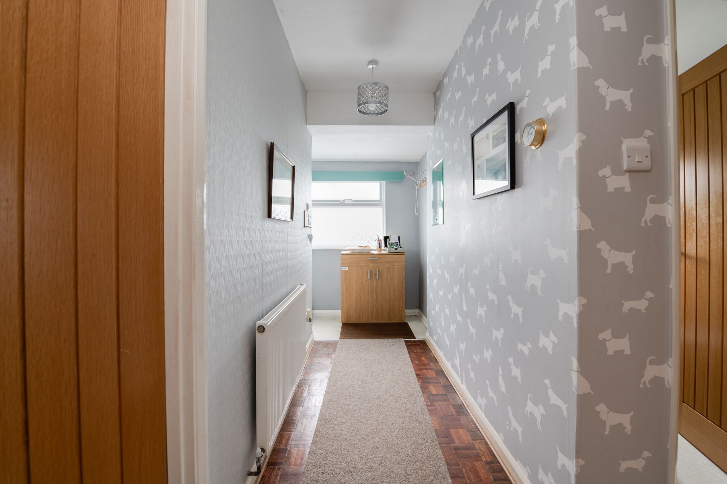 A hallway with wooden paneling, a radiator, a rug, and a wall with dog patterns.