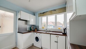 Cocina compacta con muebles blancos, lavadora integrada, un lavabo y una ventana con vistas a casas.