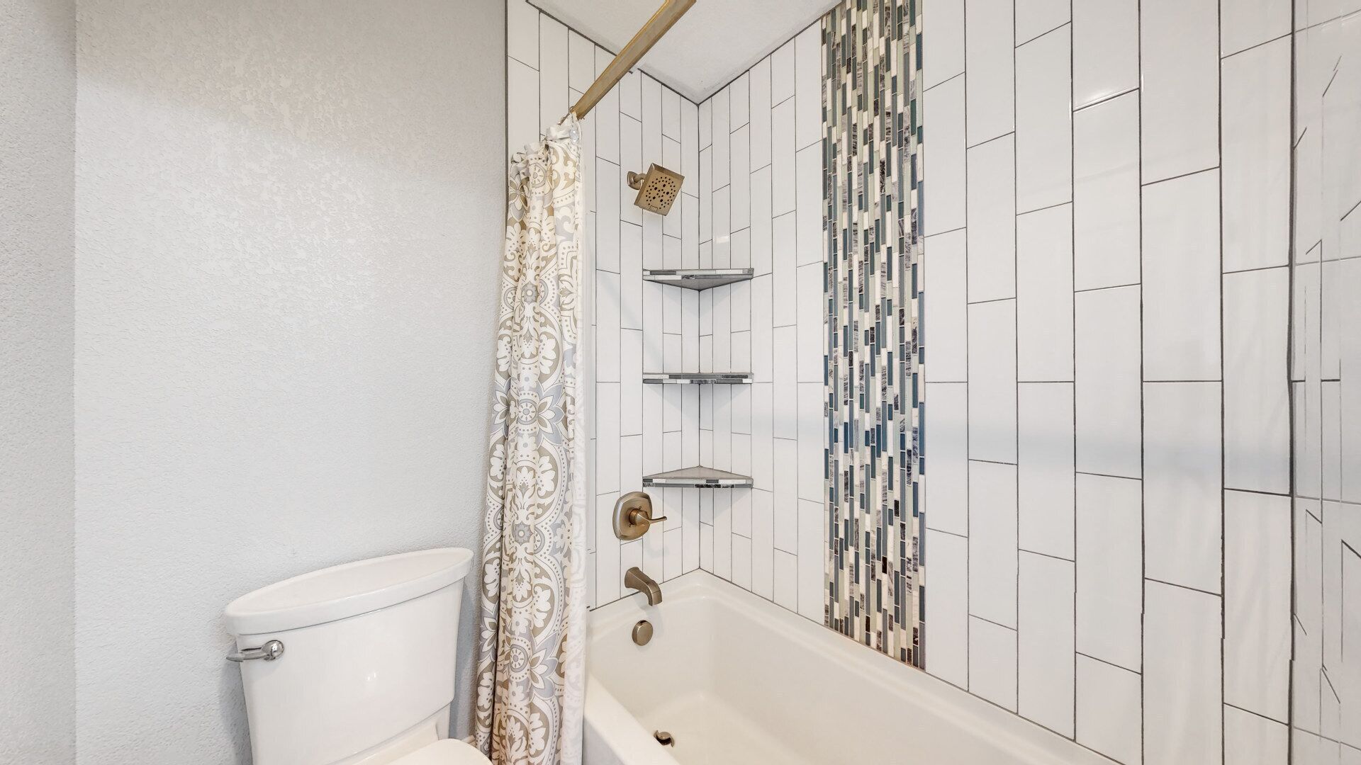 A bathroom with a toilet, a shower with a curtain, a bathtub, and a tiled wall with a mosaic pattern.