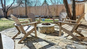 Eine Terrasse mit Adirondack-Stühlen, einer Steinkaminfeuerstelle und einem Holzzaun im Hintergrund.