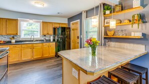A modern kitchen with wooden cabinets, a central island, and built-in shelves. - Pet-Friendly Pensacola Home w/ Sunny Backyard! (Pensacola)