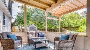 A covered patio with wicker furniture, a glass table, and a view of a house and hammock in the background. - Pet-Friendly Pensacola Home w/ Sunny Backyard! (Pensacola)