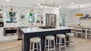 Une cuisine moderne dotée d’un îlot central, de tabourets de bar et d’un coin repas agrémenté d’un lustre.
