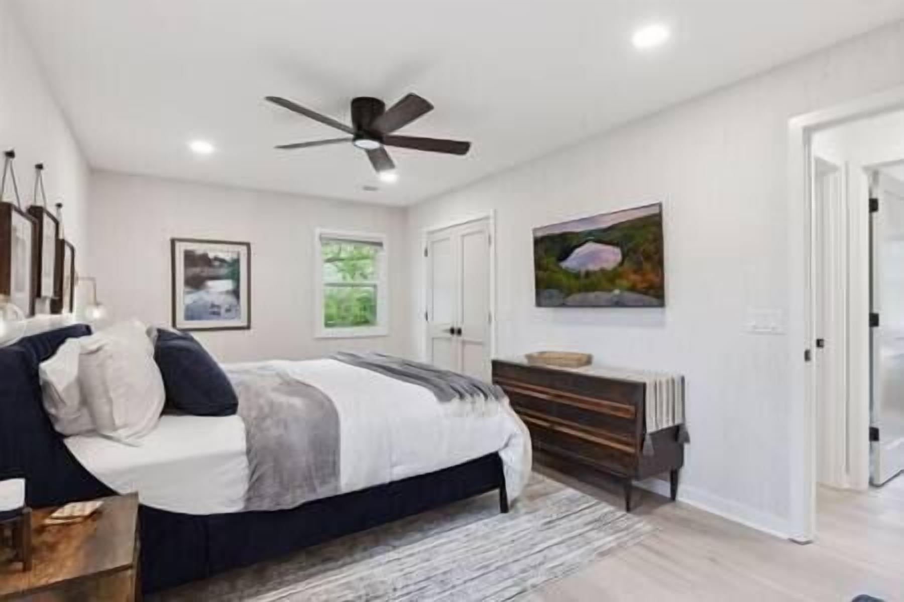 A bedroom with a bed, a ceiling fan, a dresser, and a painting on the wall.