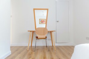 A room with a wooden desk, a chair, a door, and a wall-mounted picture.