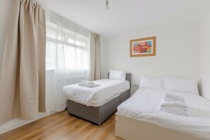 A hotel room with a bed, a bedside table, a window with curtains, and a painting on the wall.