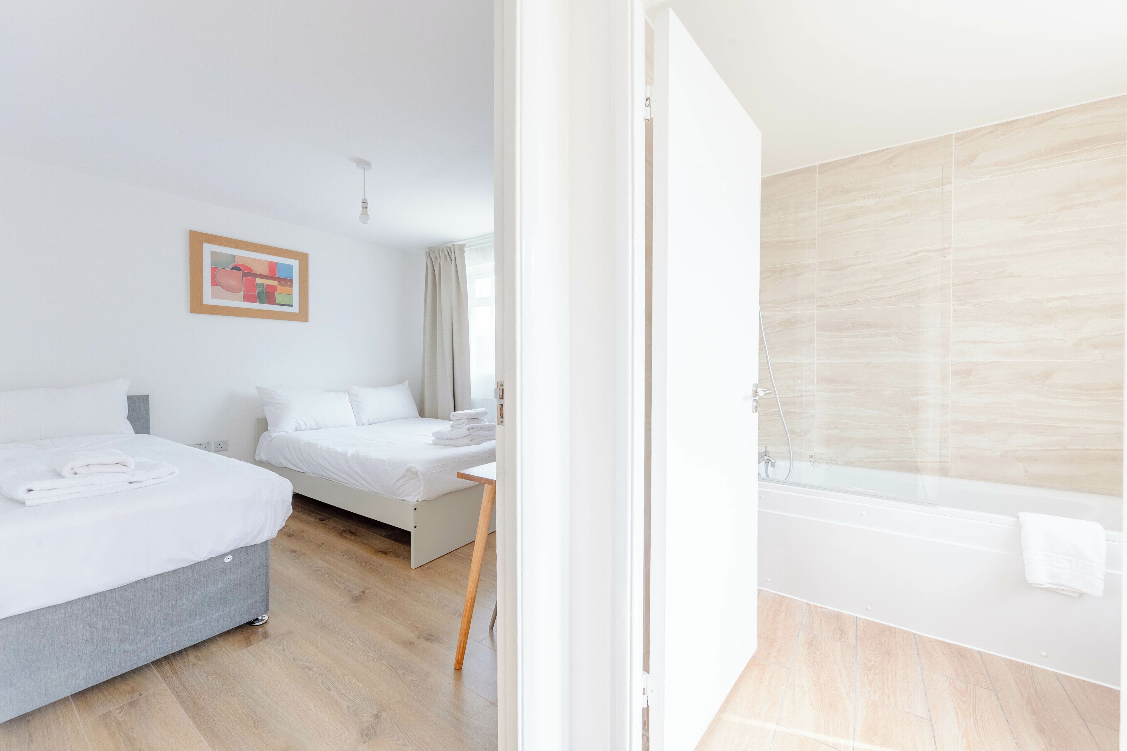 Habitación de hotel con dos camas, piso de madera, baño con bañera y un cuadro en la pared.