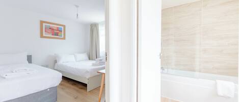 Habitación de hotel con dos camas, piso de madera, baño con bañera y un cuadro en la pared.