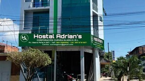 Een modern gebouw met een bord voor Hostal Adrian's. Het heeft meerdere verdiepingen en een groen-wit kleurenschema.