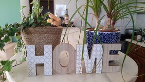 A kitchen counter with two potted plants, a bottle of wine, and the word "HOME" spelled out in wooden letters. - Arlozorov 3BD Apartment (Tel Aviv)