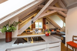 Une cuisine moderne dotée d’une cuisinière intégrée, un coin repas avec une table en bois et un espace salon confortable avec un canapé et un fauteuil.