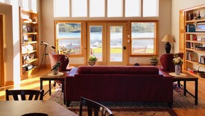 Ein gemütliches Wohnzimmer mit einem roten Sofa, Holzregalen und einem großen Fenster mit Blick auf einen See.