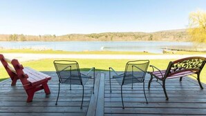 Eine Holzterrasse mit zwei roten Adirondack-Stühlen und zwei Metallstühlen mit Blick auf einen See.