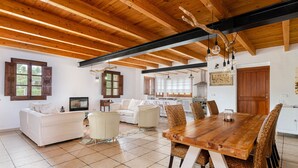 A spacious living area with a wooden ceiling, a dining table with chairs, a sofa, and a kitchen in the background. - Quiet pool villa with chill out area, barbecue near Llucmajor, YourHouse Can Rosillo (LLucmajor)