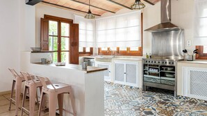 A kitchen with a large stove, wooden bar stools, and a window with blinds. - Quiet pool villa with chill out area, barbecue near Llucmajor, YourHouse Can Rosillo (LLucmajor)