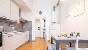 Une cuisine moderne avec des meubles en bois clair, une cuisinière à gaz et un réfrigérateur. On y trouve une table à manger avec des chaises et une petite plante en pot.