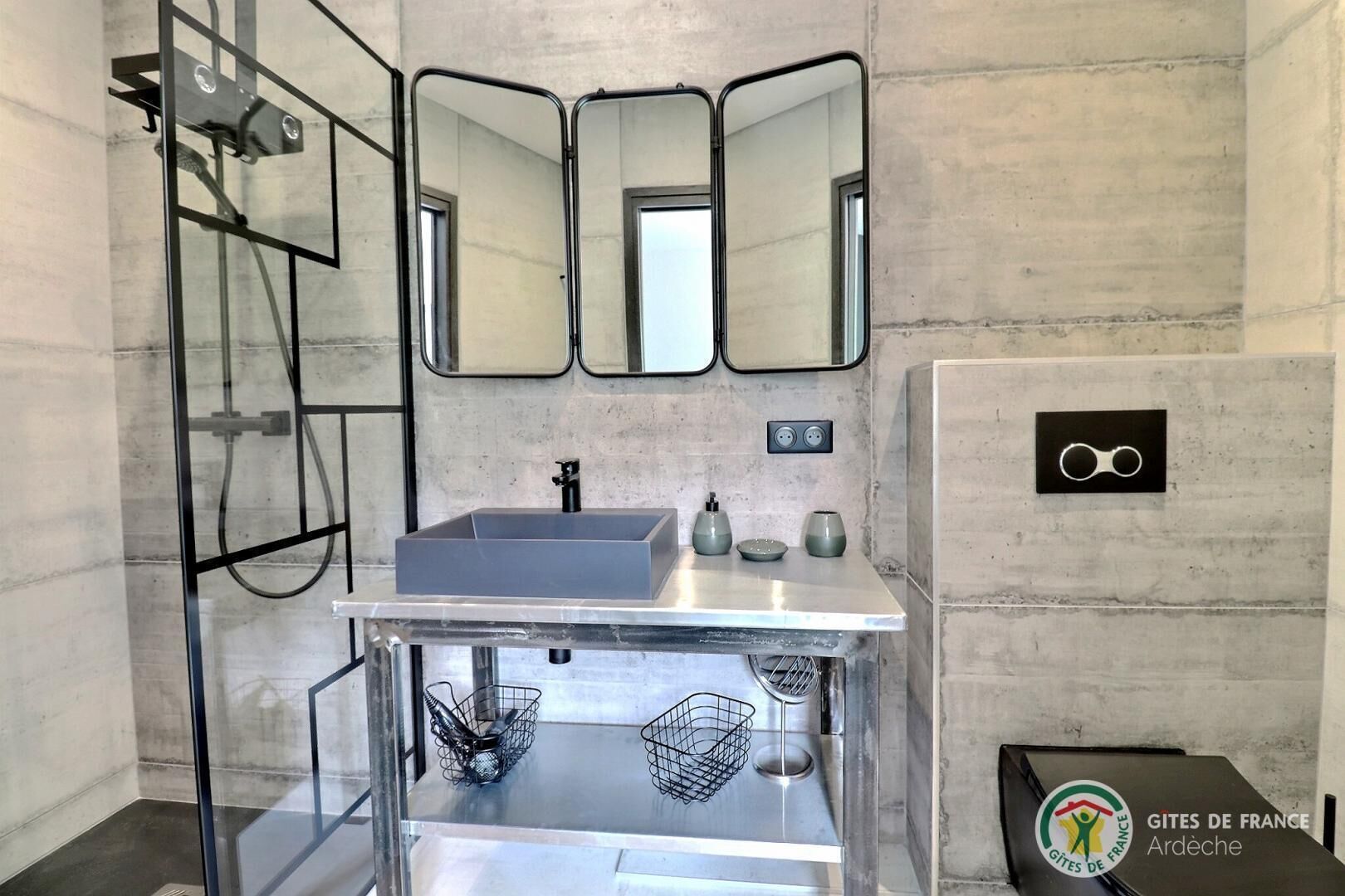 Un baño moderno con un lavabo rectangular, tres espejos, una ducha y un perchero para toallas.