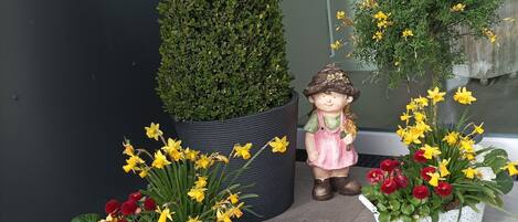 Une plante en pot avec des fleurs jaunes, une petite figurine et un grand arbuste vert.