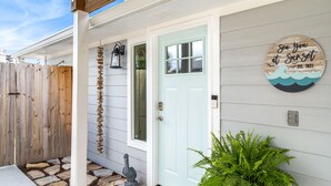 A house with a light blue door, a wooden fence, a welcome mat, and a sign on the wall. - New Reno! Optional htd private Pool! Close to Bch! Pet Friendly! Putting green! (Panama City Beach)
