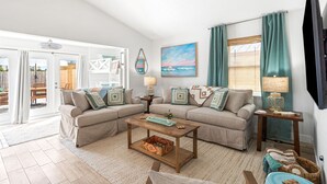 A living room with a sectional sofa, a coffee table, a TV, and a view of the outdoors. - New Reno! Optional htd private Pool! Close to Bch! Pet Friendly! Putting green! (Panama City Beach)