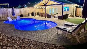A backyard with a swimming pool, lounge chairs, a covered patio, and a TV screen. - New Reno! Optional htd private Pool! Close to Bch! Pet Friendly! Putting green! (Panama City Beach)