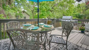 A covered outdoor patio with a table set for dining, surrounded by chairs, and a grill in the background.