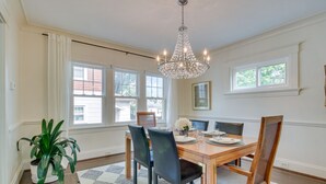 A dining room with a wooden table, four chairs, a chandelier, and large windows.