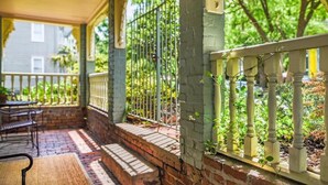 A covered porch with a brick floor, a wooden table, and a metal fence. - Catherine Ward House Inn (Savannah)