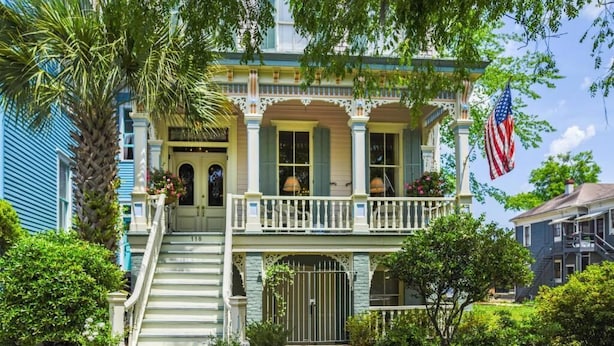 A two-story house with a porch, a flag, and a staircase leading to the entrance. - Catherine Ward House Inn (Savannah)