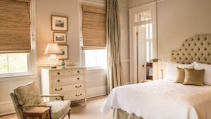 A bedroom with a large bed, a dresser, a chair, and a window with blinds. - Catherine Ward House Inn (Savannah)