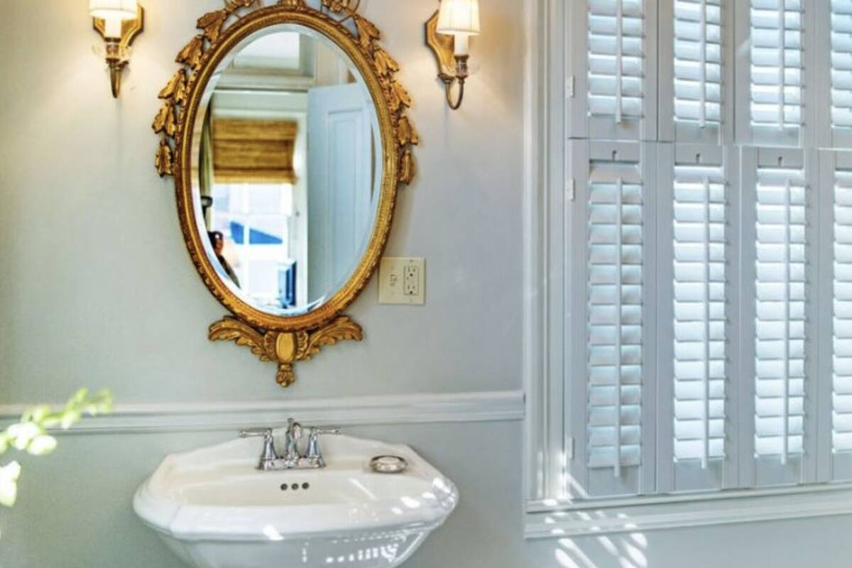 A bathroom with a white sink, gold-framed mirror, and wall-mounted sconces.