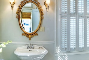 A bathroom with a white sink, gold-framed mirror, and wall-mounted sconces. - Catherine Ward House Inn (Savannah)