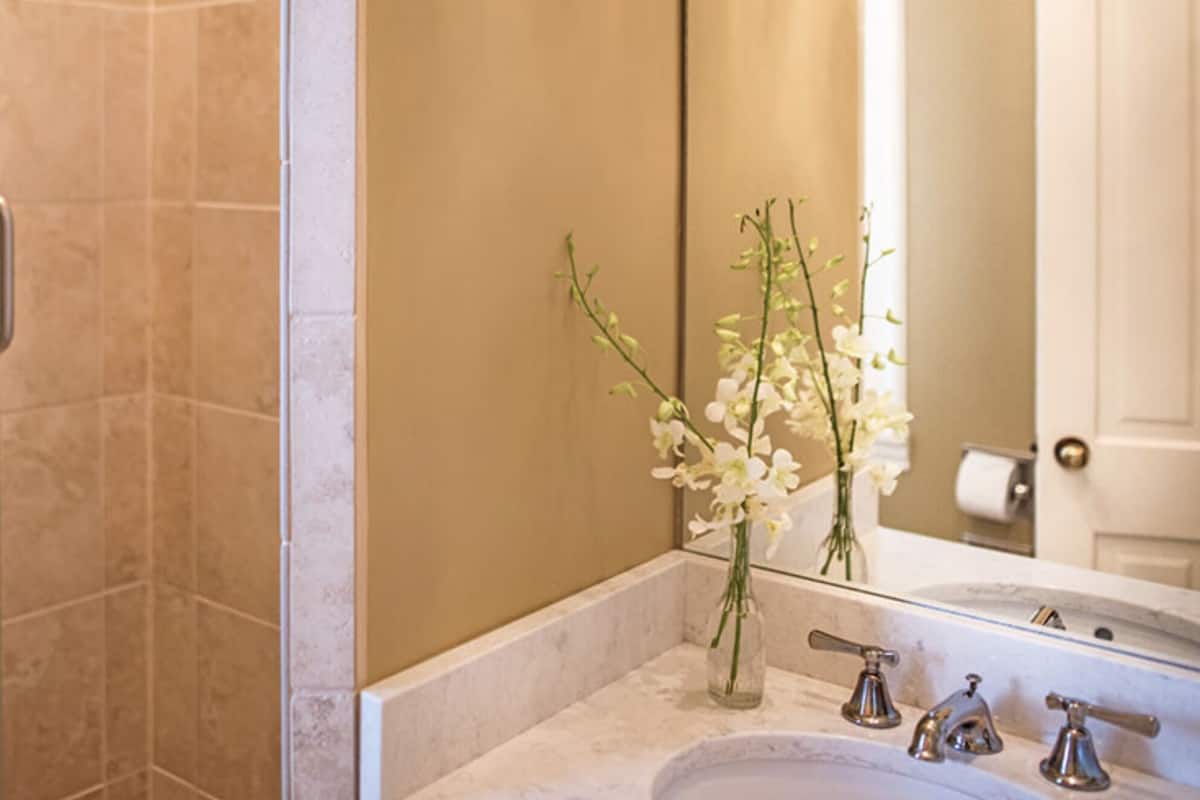 A bathroom with a glass shower door, a marble sink, and a vase with white flowers.