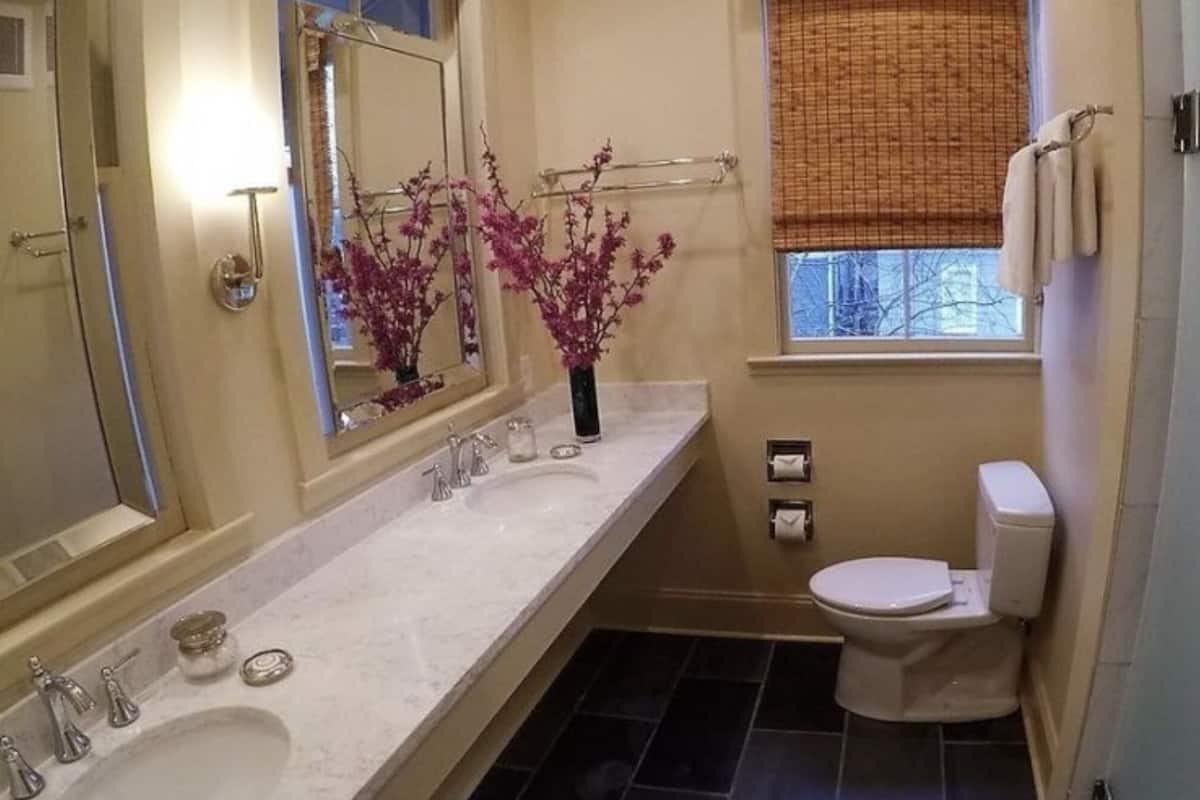 A bathroom with a sink, mirror, toilet, and window with a view.