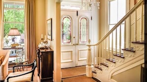 A grand entrance with a staircase, a chandelier, and a view of greenery outside. - Catherine Ward House Inn (Savannah)
