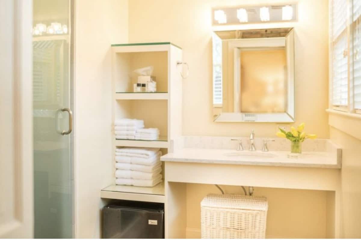 A bathroom with a glass shower door, a white sink with a mirror, and a wicker basket.