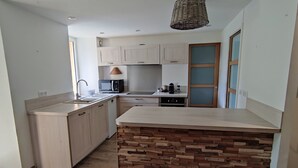 Una cocina moderna con armarios de madera clara, una isla central con salpicadero tipo piedra y una lámpara colgante.