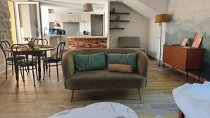 Una sala de estar moderna con un sofá, una mesa de comedor y sillas. Se observa una cocina al fondo con armarios y una encimera.
