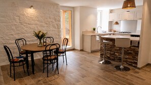 A modern kitchen with a dining area, featuring a wooden table, chairs, and a bar stool.