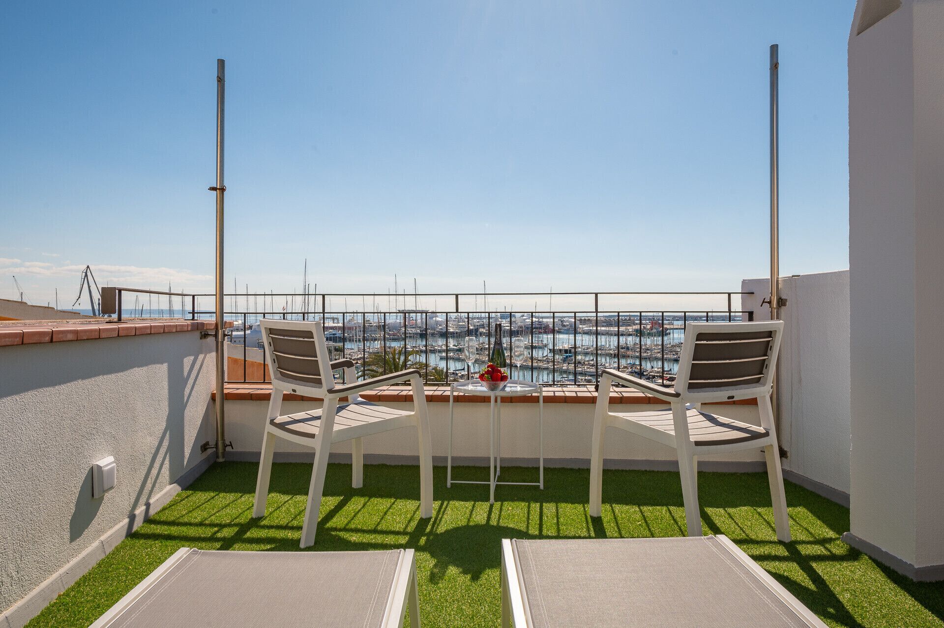 A balcony with two white chairs, a small round table, and a view of a marina.