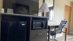 A kitchenette with a microwave, refrigerator, and a flat-screen TV. There is a dining table with chairs and a lamp. - Harrington Welcome Inn (Harrington)
