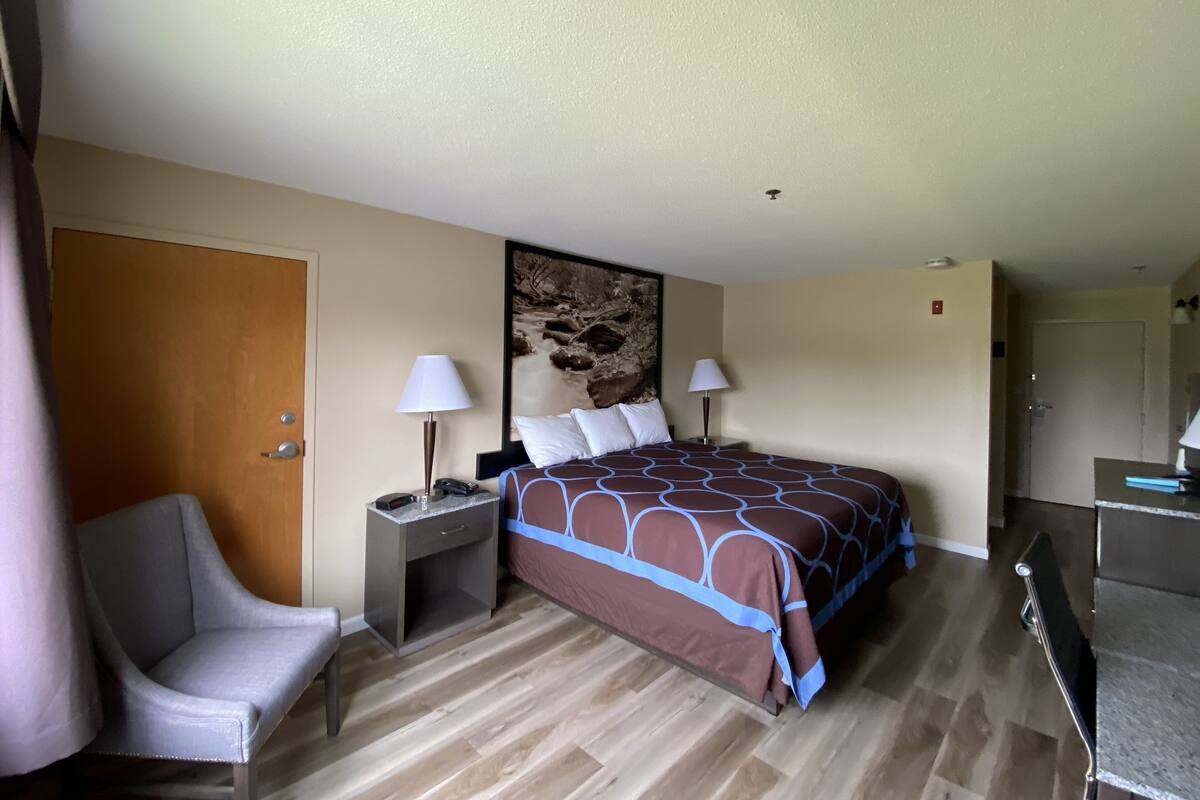A hotel room with a bed, a desk, a chair, and a painting on the wall.