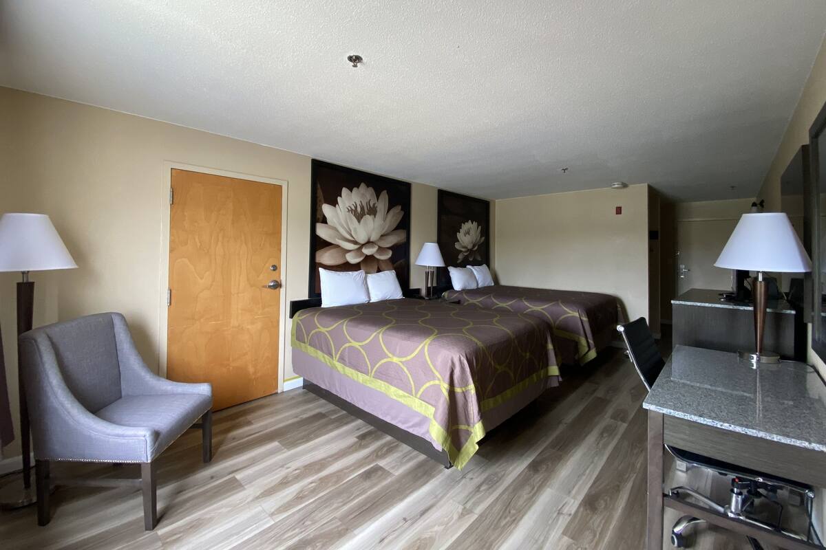 A hotel room with two beds, a desk, a chair, and a bathroom.