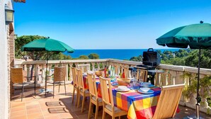A terrace with a table set for dining, outdoor umbrellas, and a grill.