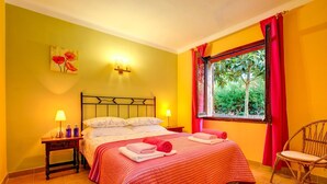 A room with a bed, a nightstand, a chair, and a window with curtains. - Níspero - Two Bedroom Villa, Sleeps 4 (Begur)